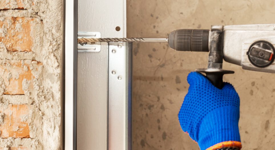 Garage doors installation. Worker drills a hole for the bolt IDC